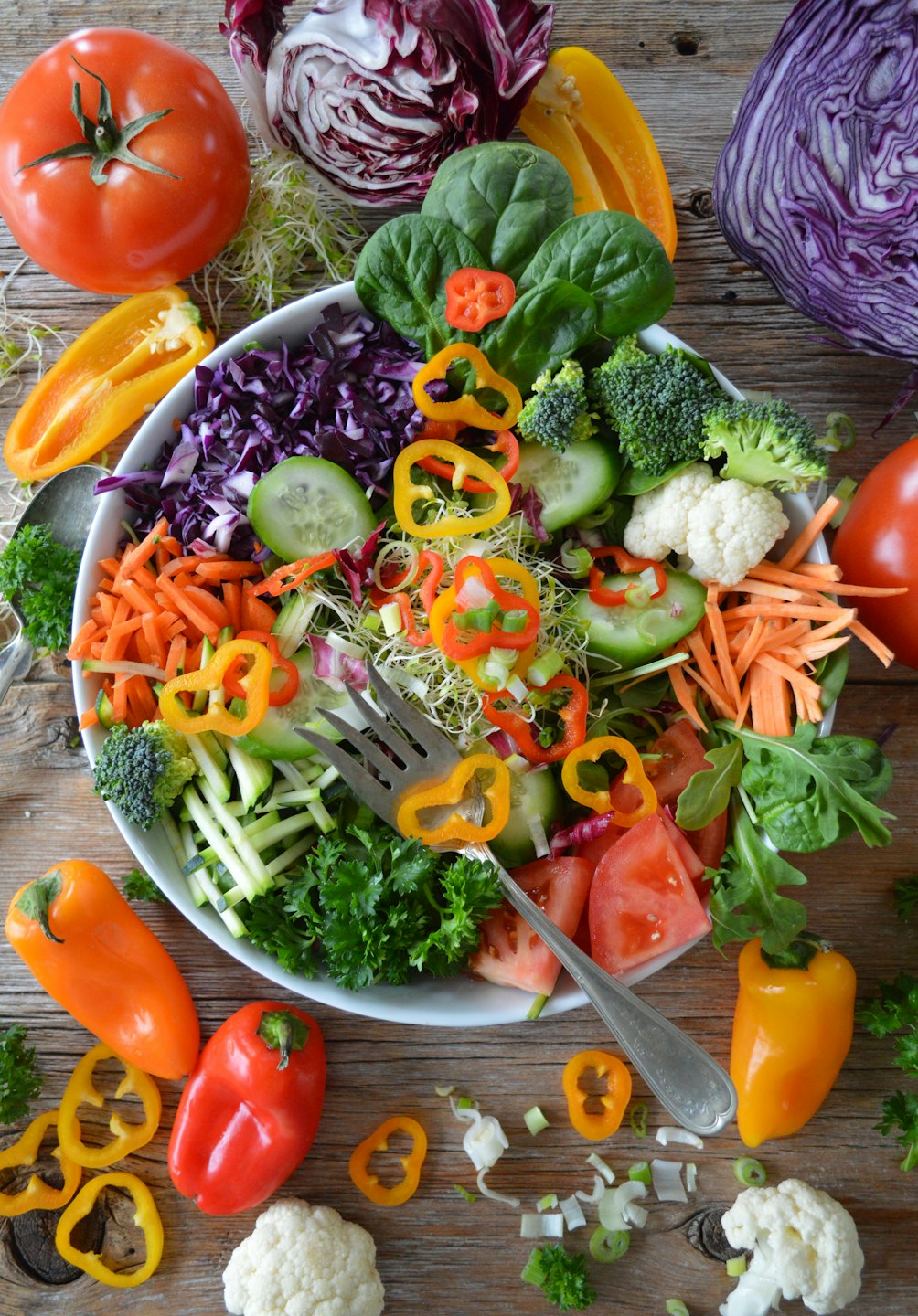 Färsk sallad i en vit skål med en gaffel på ett träbord.