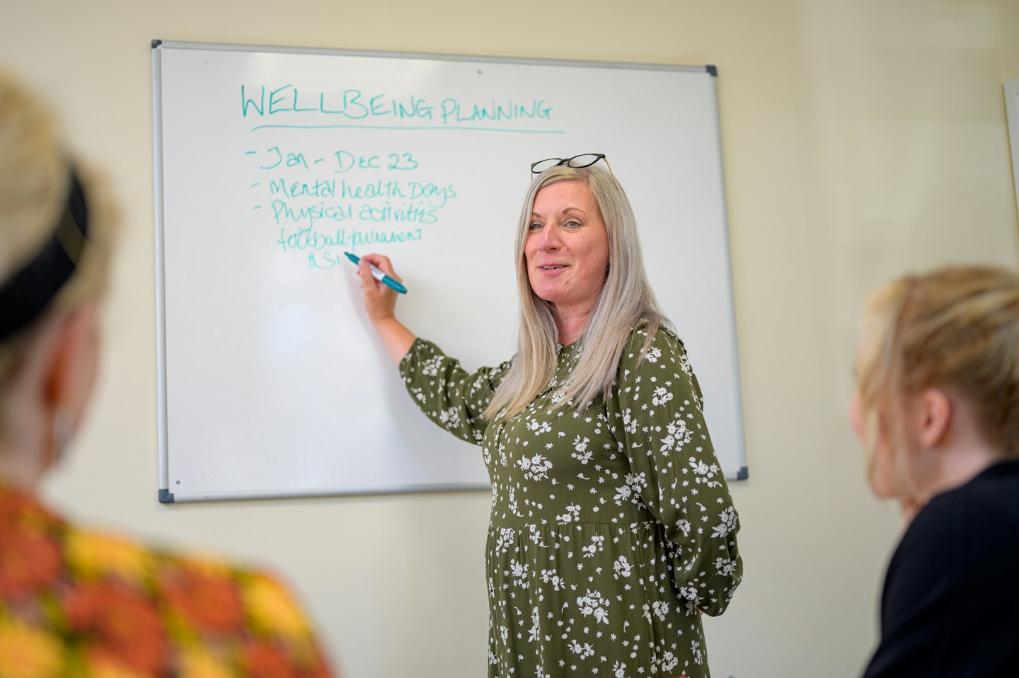 Kvinna i grön klänning leder planeringssession för välbefinnande vid whiteboard.